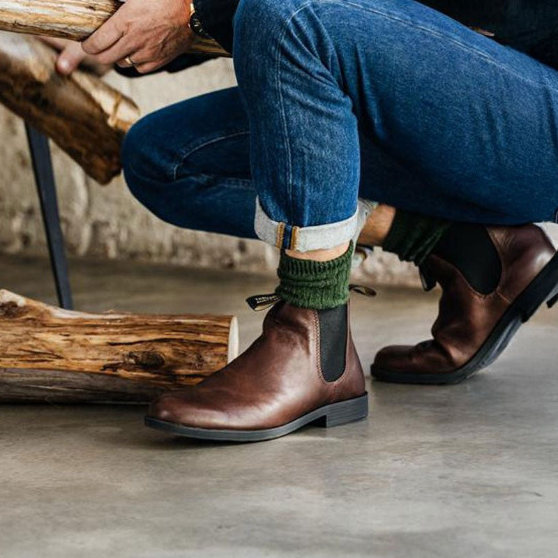 Person in jeans crouching by a log pile wearing brown Blundstone Chelsea boots