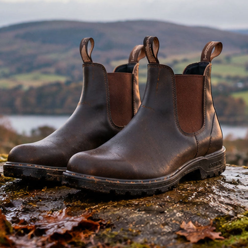 Pair of brown Blundstone Chelsea boots on a rock with autumn countryside behind