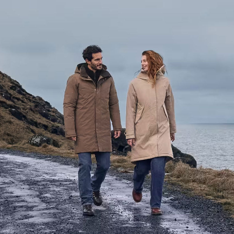 Man and woman wearing Didriksons waterproof parkas walking along a coastal road