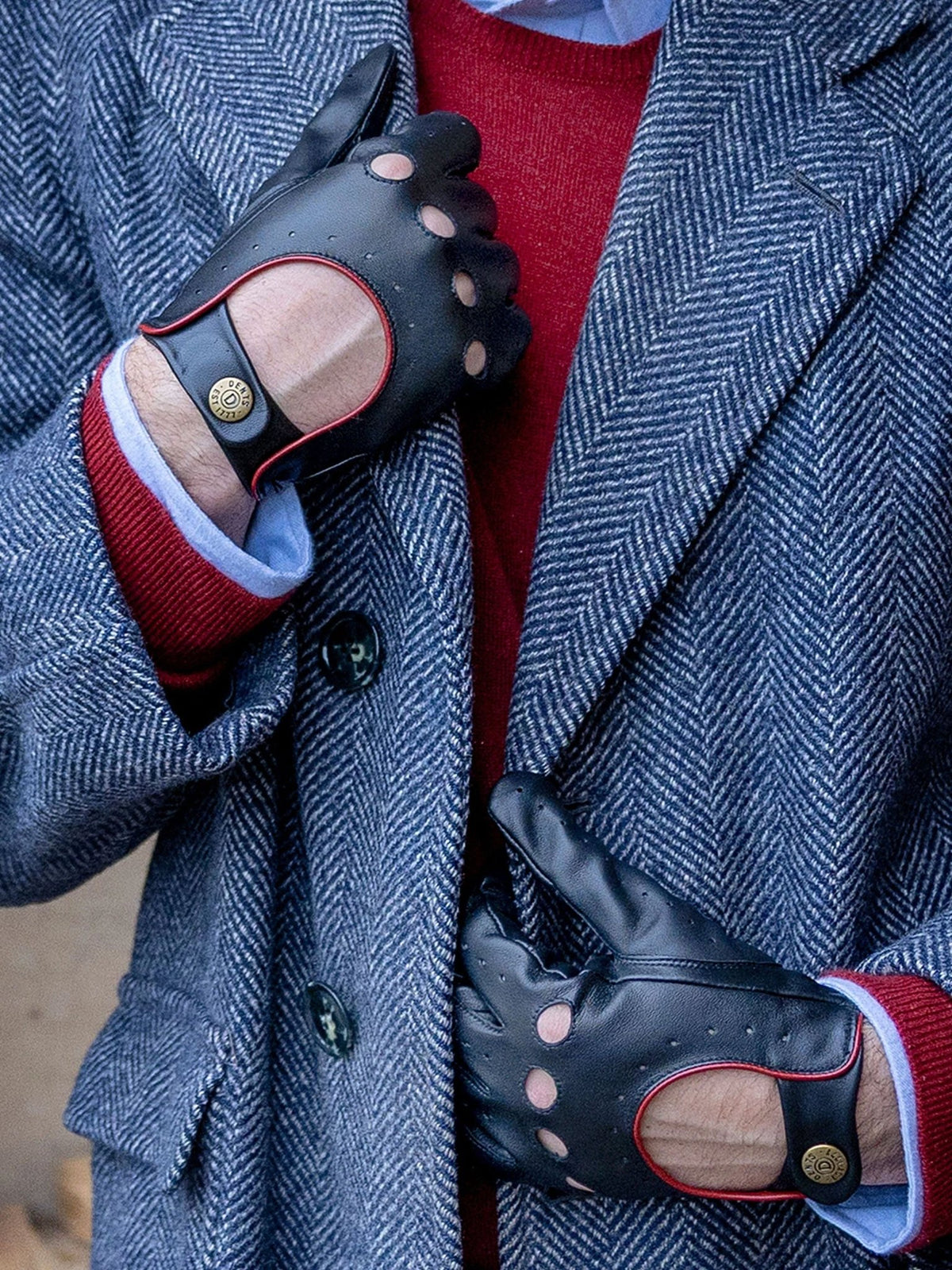 Dents Delta men's black leather driving gloves with berry red trim, worn with a blue herringbone coat