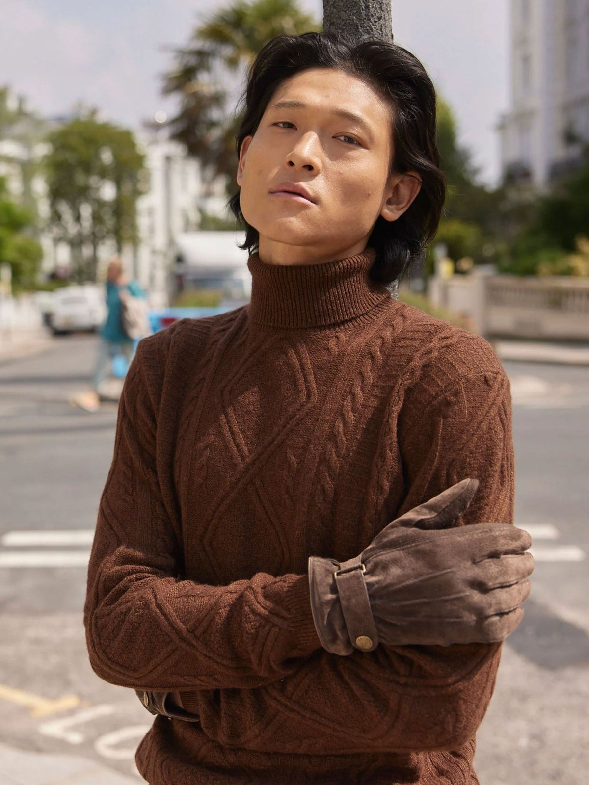 Man wearing Dents brown suede touchscreen gloves with a rust cable-knit roll neck jumper in the street