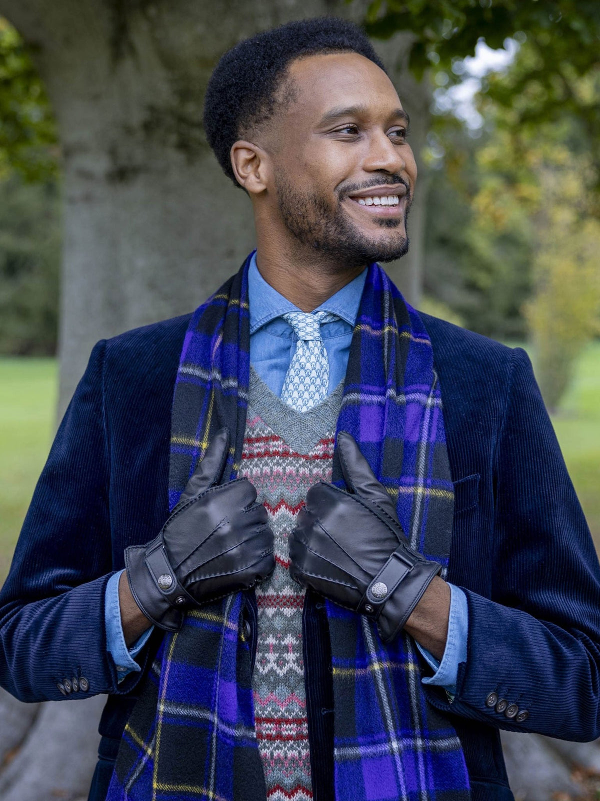 Man wearing Dents Tetbury black leather gloves with a navy coat and tartan scarf in a park