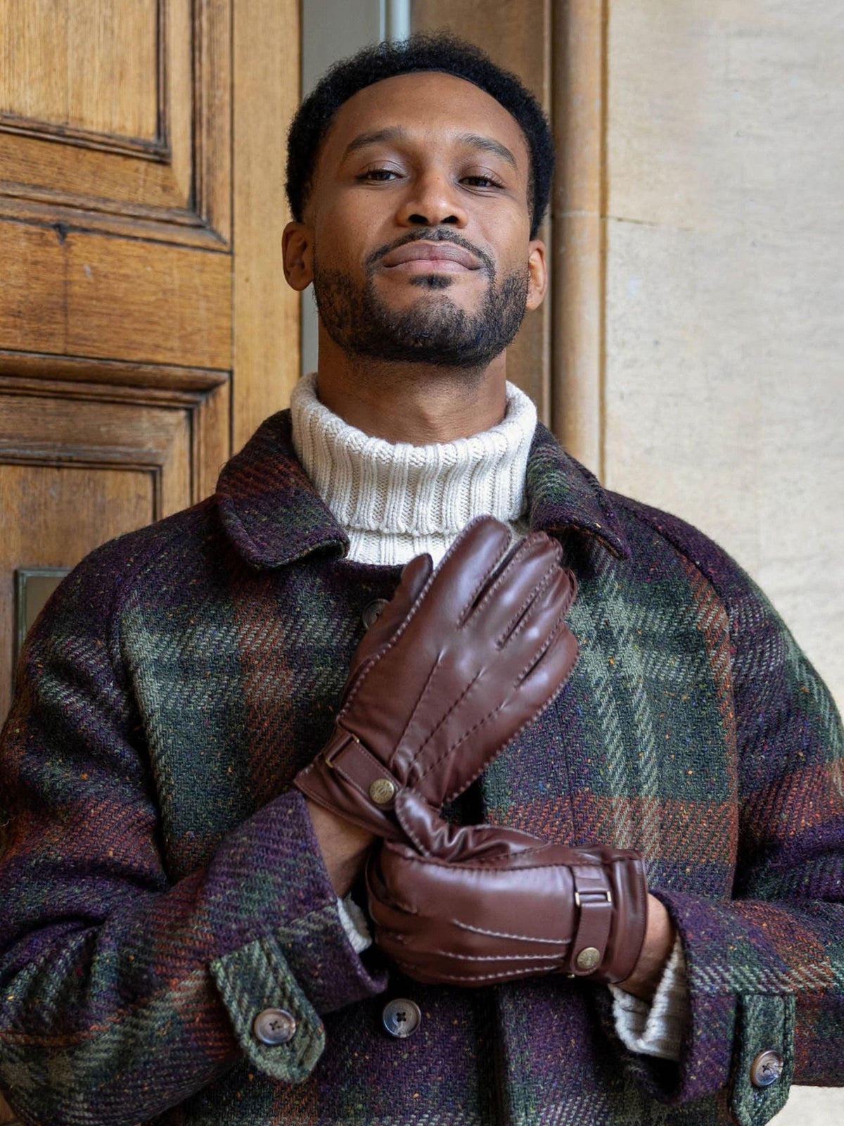 Man wearing Dents Tetbury brown leather gloves with a green check coat and white roll neck