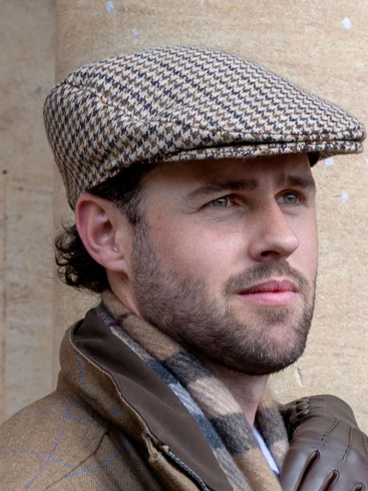 Dents Blashford men's brown dogtooth tweed flat cap, close-up worn with a scarf