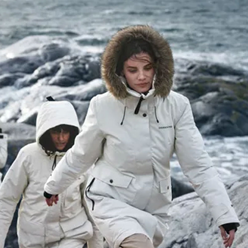 Woman in a white Didriksons parka with fur-trim hood on a rocky coast