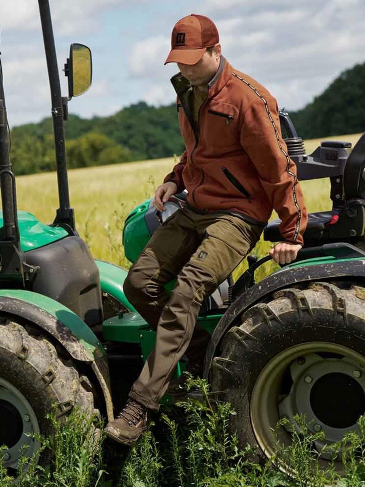 Man wearing Härkila Scandinavian Trousers stepping off a tractor – mens field and work trousers