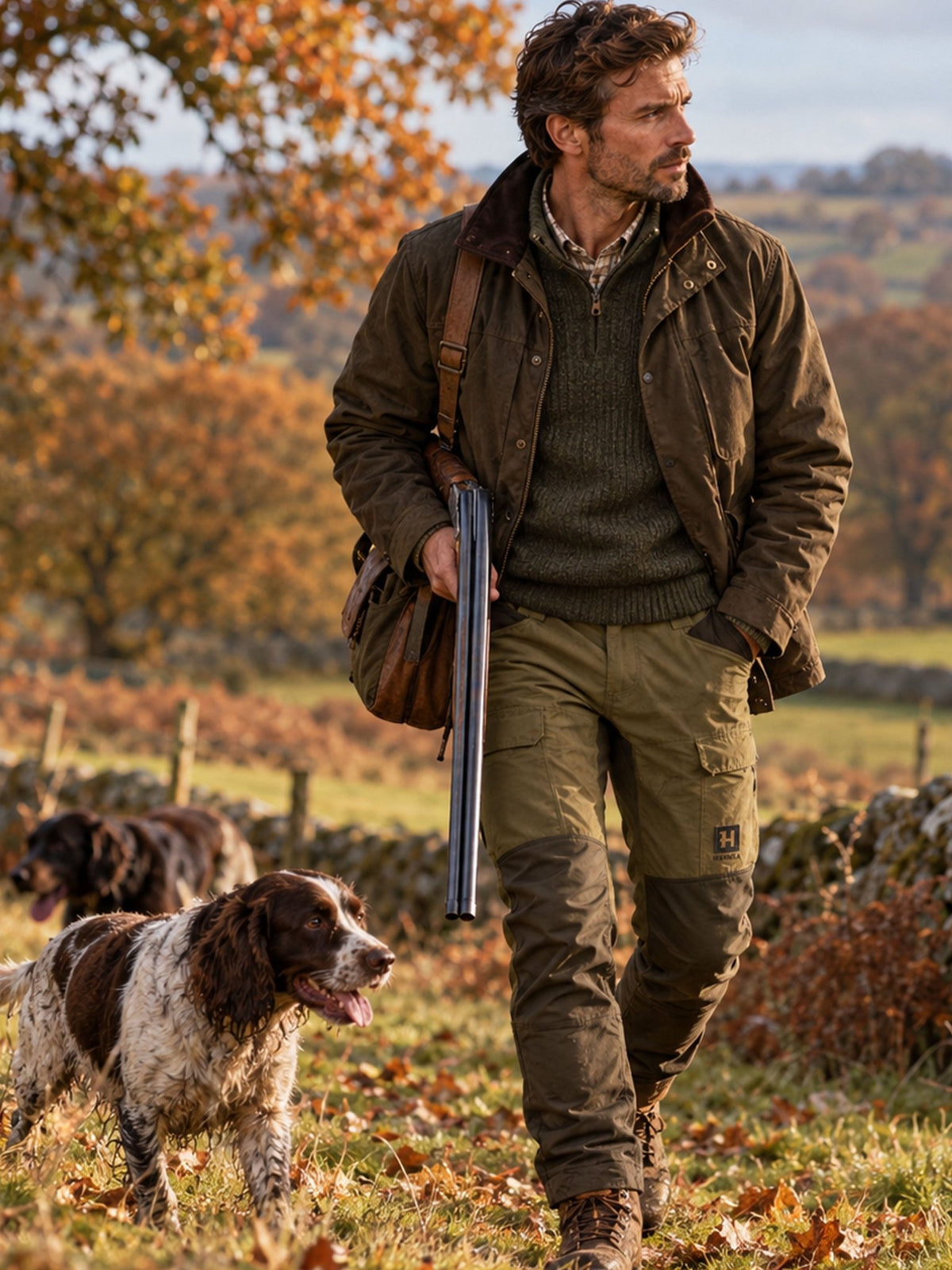 Man wearing Härkila Scandinavian Trousers in green carrying a shotgun with two spaniels – mens hunting trousers