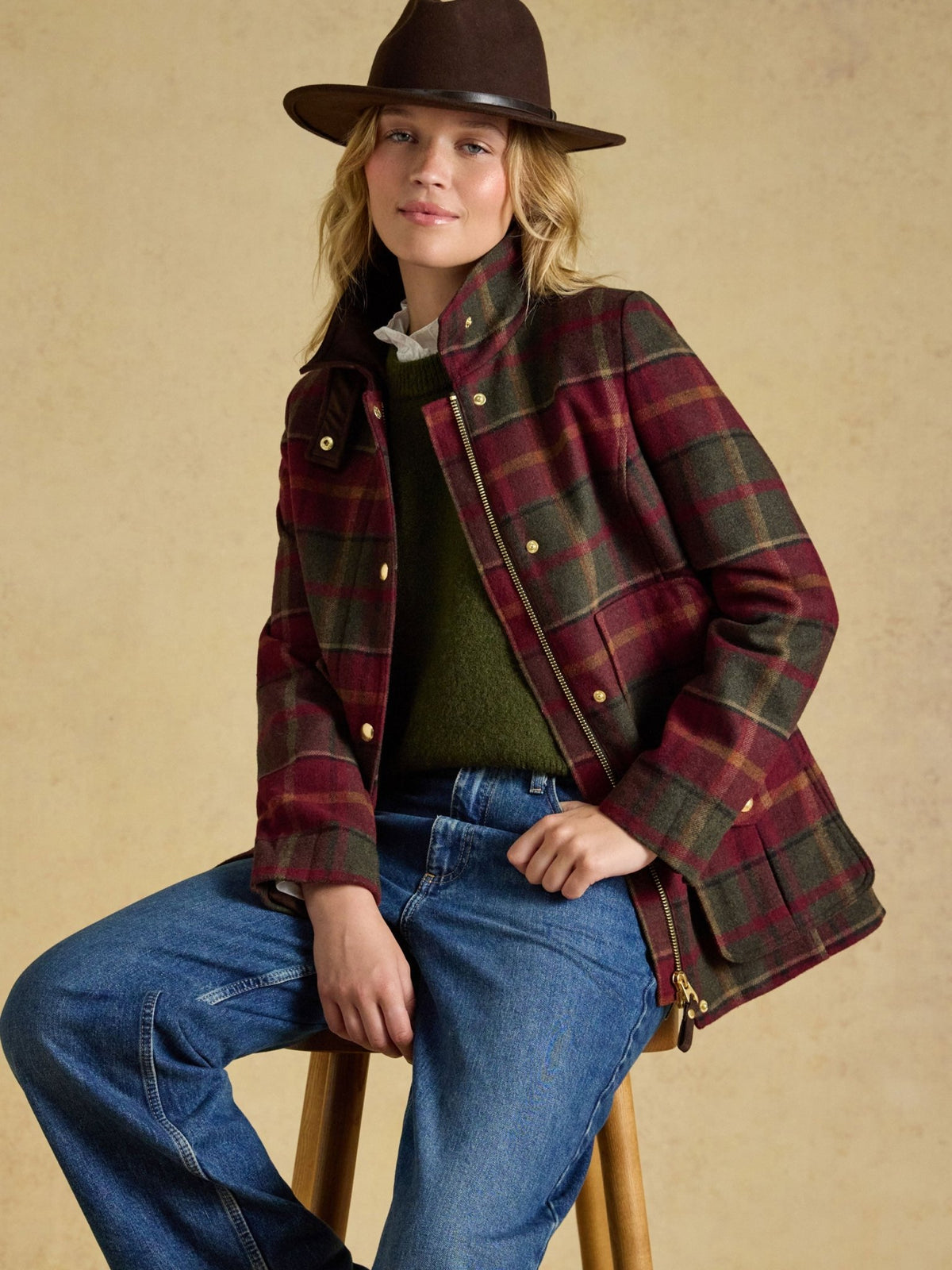 Joules ladies fieldcoat in red and green check tweed worn with jeans and a brown hat, lifestyle view
