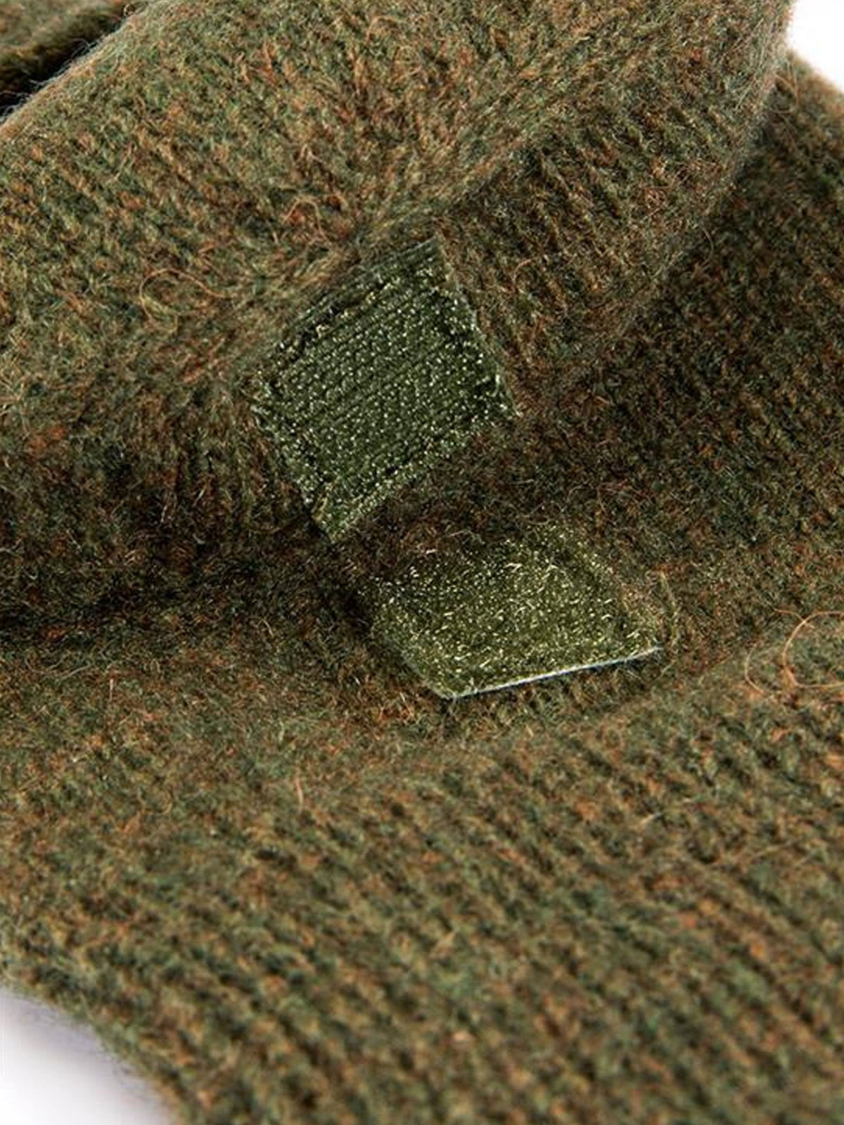 Close-up of the olive marl knitted wool fabric and cap fastening tab on Dents shooting gloves