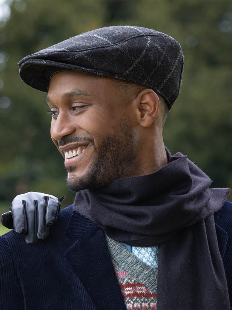 Dents men's charcoal windowpane check tweed flat cap, side view worn with navy coat and scarf