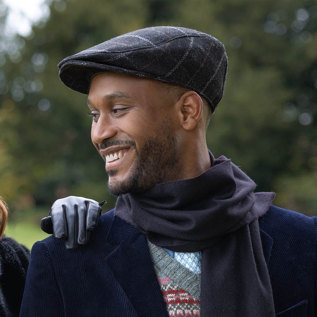 Dents men's charcoal windowpane check tweed flat cap, side view worn with navy coat and scarf