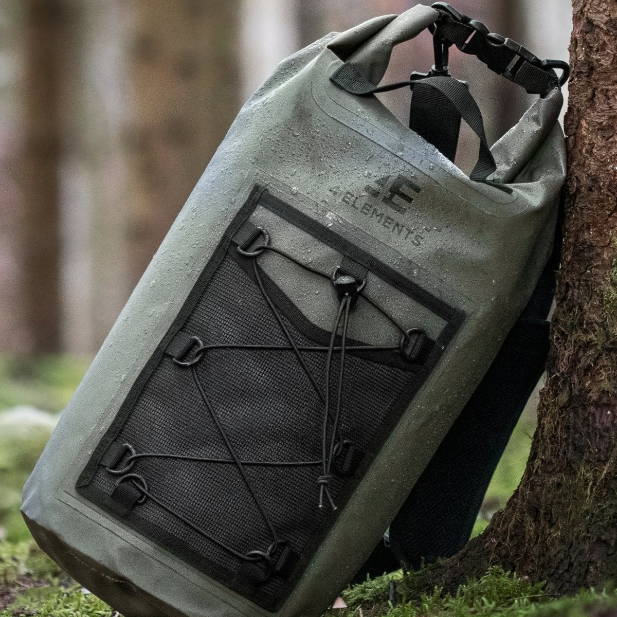 4 Elements 20L Waterproof Dry Bag Rucksack in green - close-up leaning against a tree trunk with water droplets on the fabric