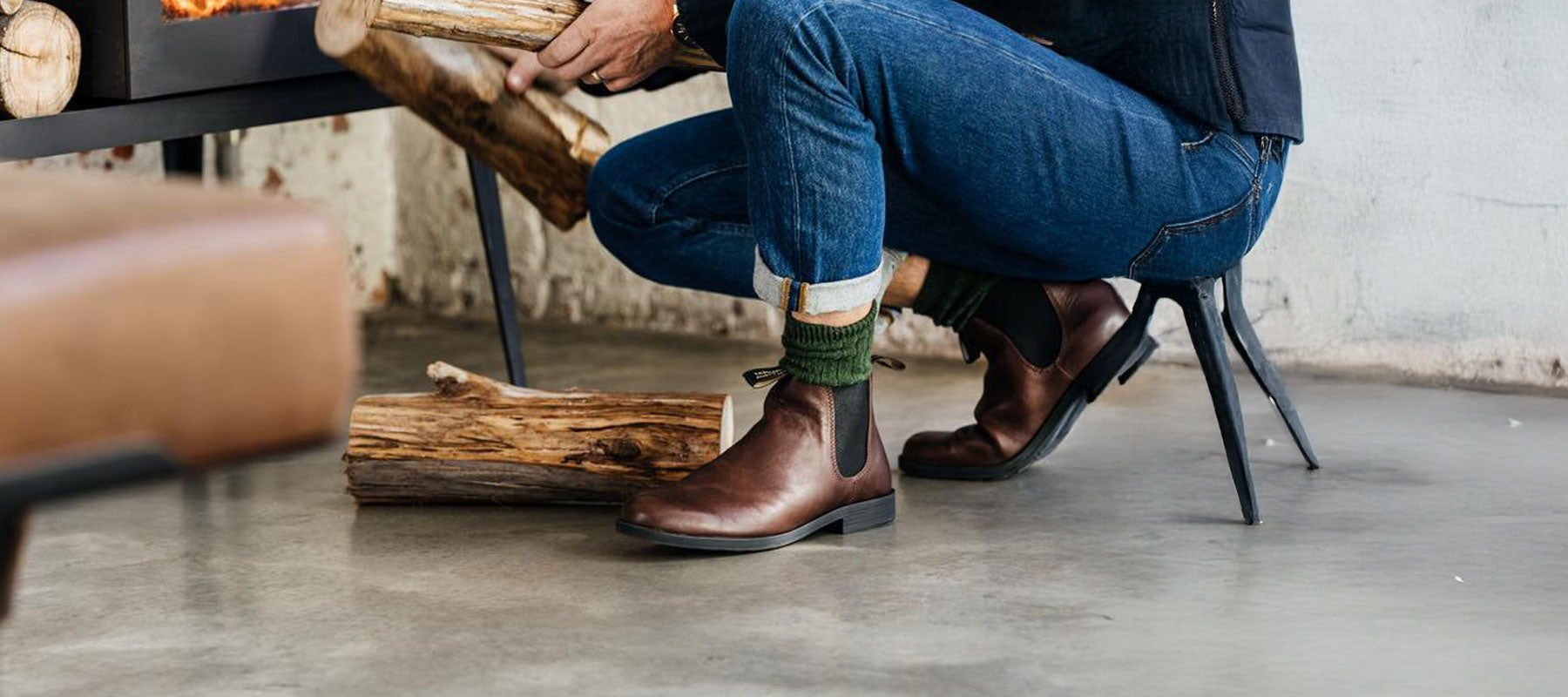 Person in jeans crouching by a log pile wearing brown Blundstone Chelsea boots