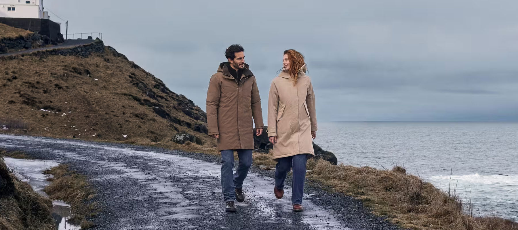 Man and woman wearing Didriksons waterproof parkas walking along a coastal road