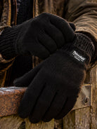 Dents Durham men's black Thinsulate knitted gloves, worn with waxed jacket on a wooden gate