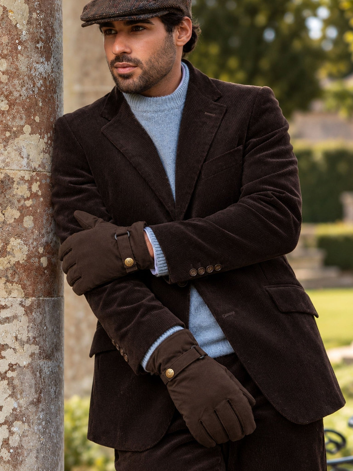 Man wearing Dents brown waxed cotton gloves with a brown corduroy jacket and flat cap outdoors