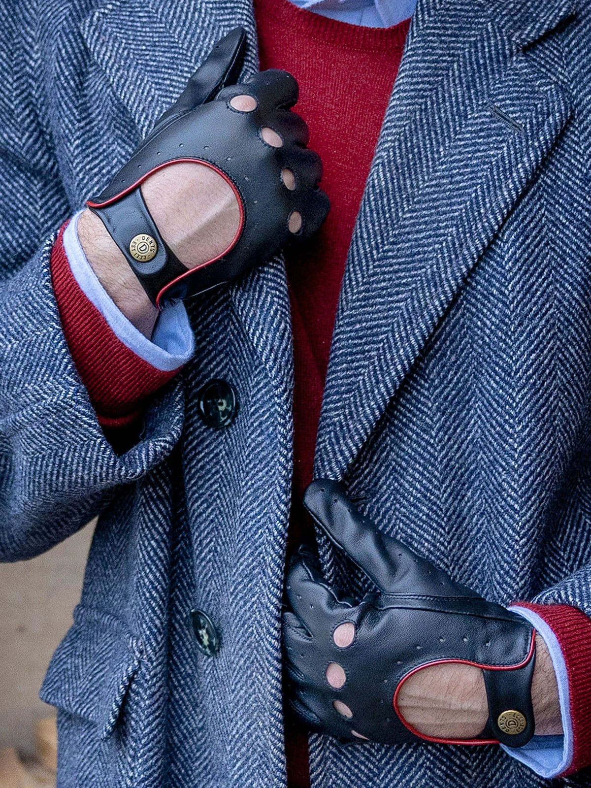 Dents Delta men's black leather driving gloves with berry red trim, worn with a blue herringbone coat