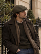 Dents Grafham men's chocolate brown micro-herringbone tweed flat cap, worn with long coat and scarf in the street