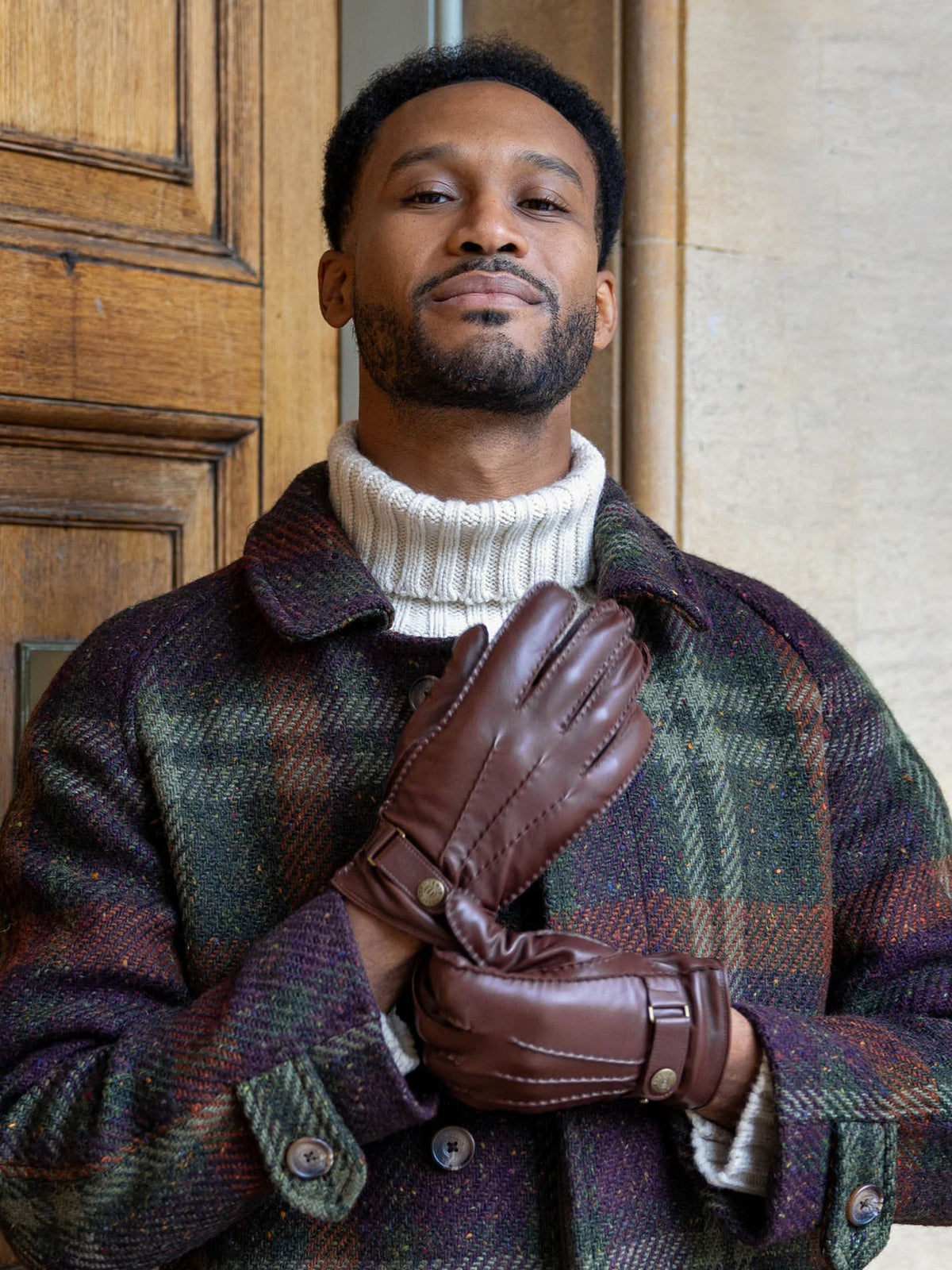 Man wearing Dents Tetbury brown leather gloves with a green check coat and white roll neck