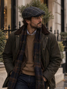 Dents Colliford men's charcoal windowpane check tweed flat cap, worn with dark coat, tartan scarf and tan jumper