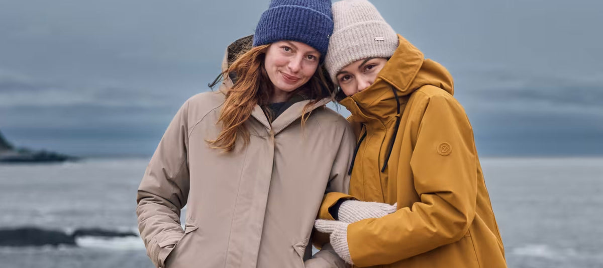 Two women wearing Didriksons winter parkas in yellow and brown with bobble hats