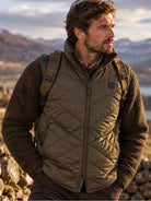 Man wearing Harkila Heat men's heated insulated waistcoat in Willow green over a fleece, lifestyle view in the hills