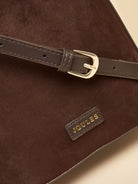 Close-up of a dark brown suede shoulder bag with a matching brown leather strap and gold-tone buckle, featuring a small gold JOULES brand patch.