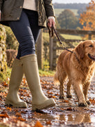 Woman walking a golden retriever on a muddy country path wearing Joules Luxe khaki green neoprene lined tall wellies