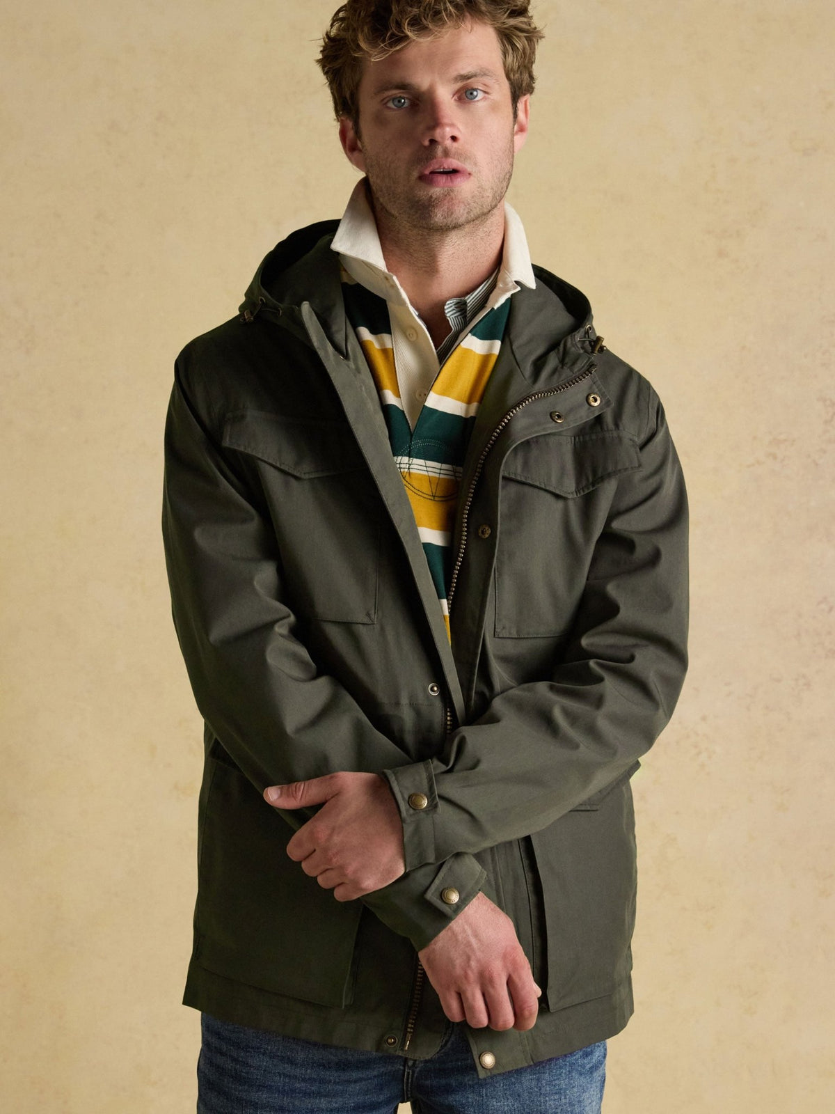 Joules men's green cotton hooded raincoat worn with striped rugby shirt, lifestyle view