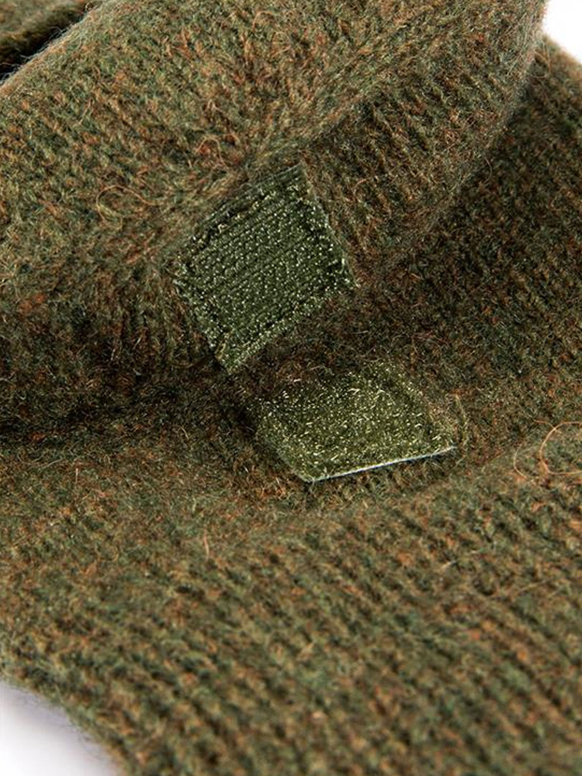 Close-up of the olive marl knitted wool fabric and cap fastening tab on Dents shooting gloves