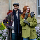 Man wearing the Dents olive windowpane check tweed flat cap with a plaid coat, outdoor lifestyle view
