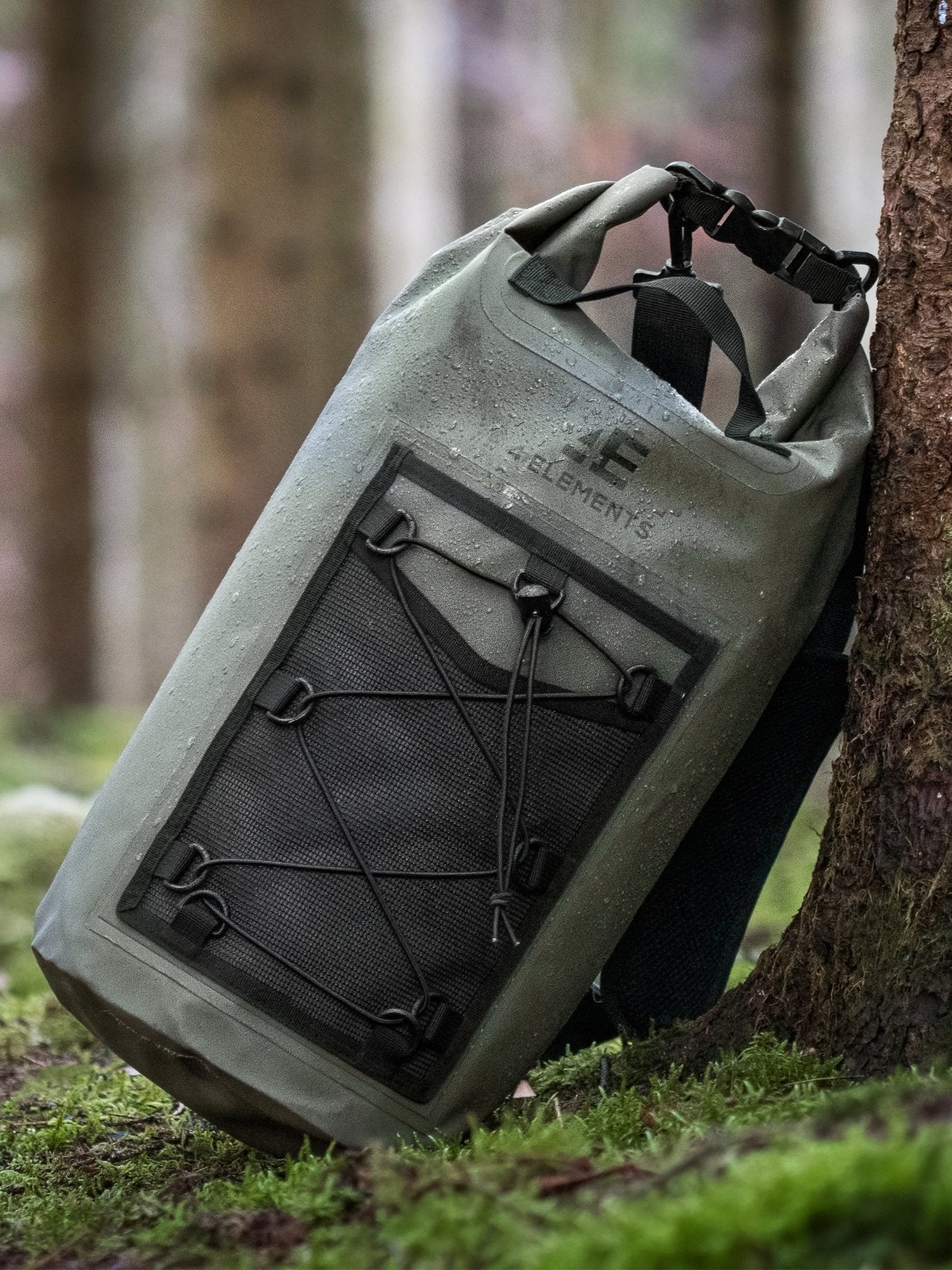 4 Elements 20L Waterproof Dry Bag Rucksack in green - close-up leaning against a tree trunk with water droplets on the fabric